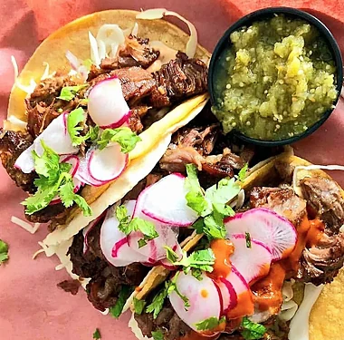 Close-up of carnitas tacos with radish, cilantro and salsa verde