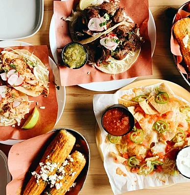A spread of tacos and sides on a wooden table at Cerdo