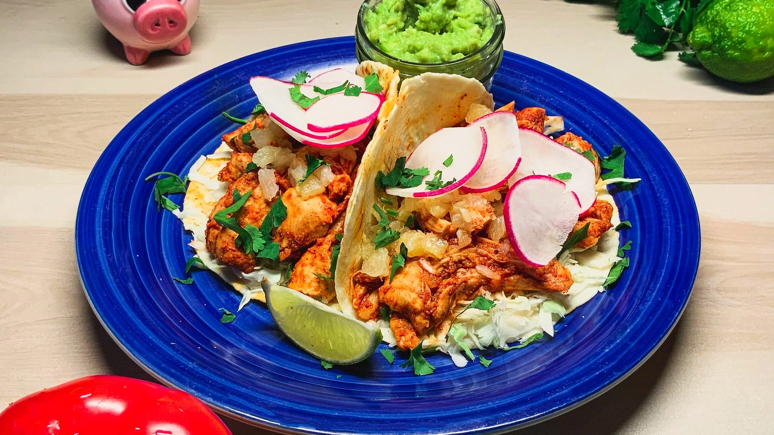 Chicken al pastor tacos with pineapple, radish and cilantro on a blue plate, with guacamole and lime