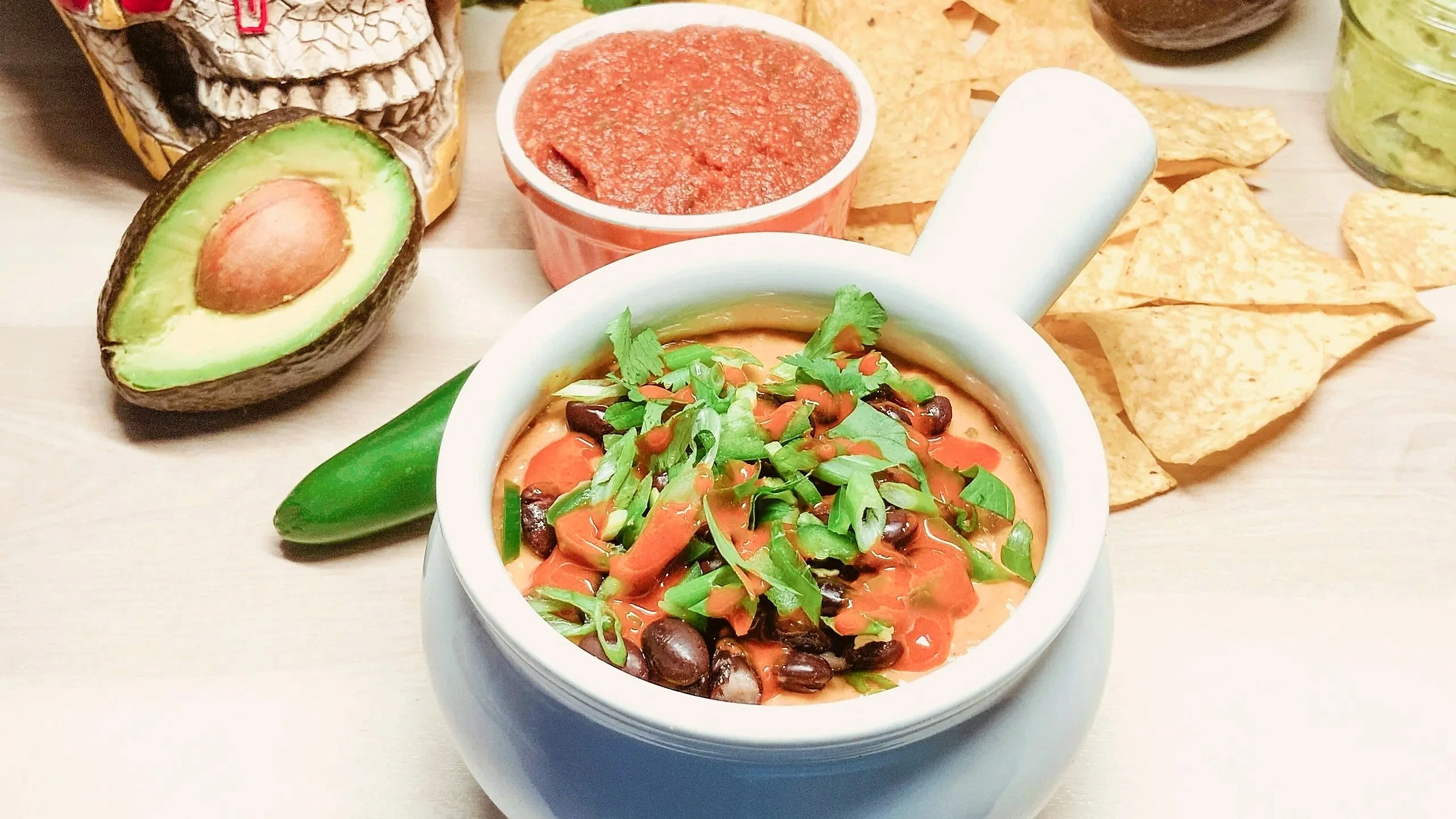 Queso fundido with black beans in a white crock, with salsa, guacamole, avocado and tortilla chips