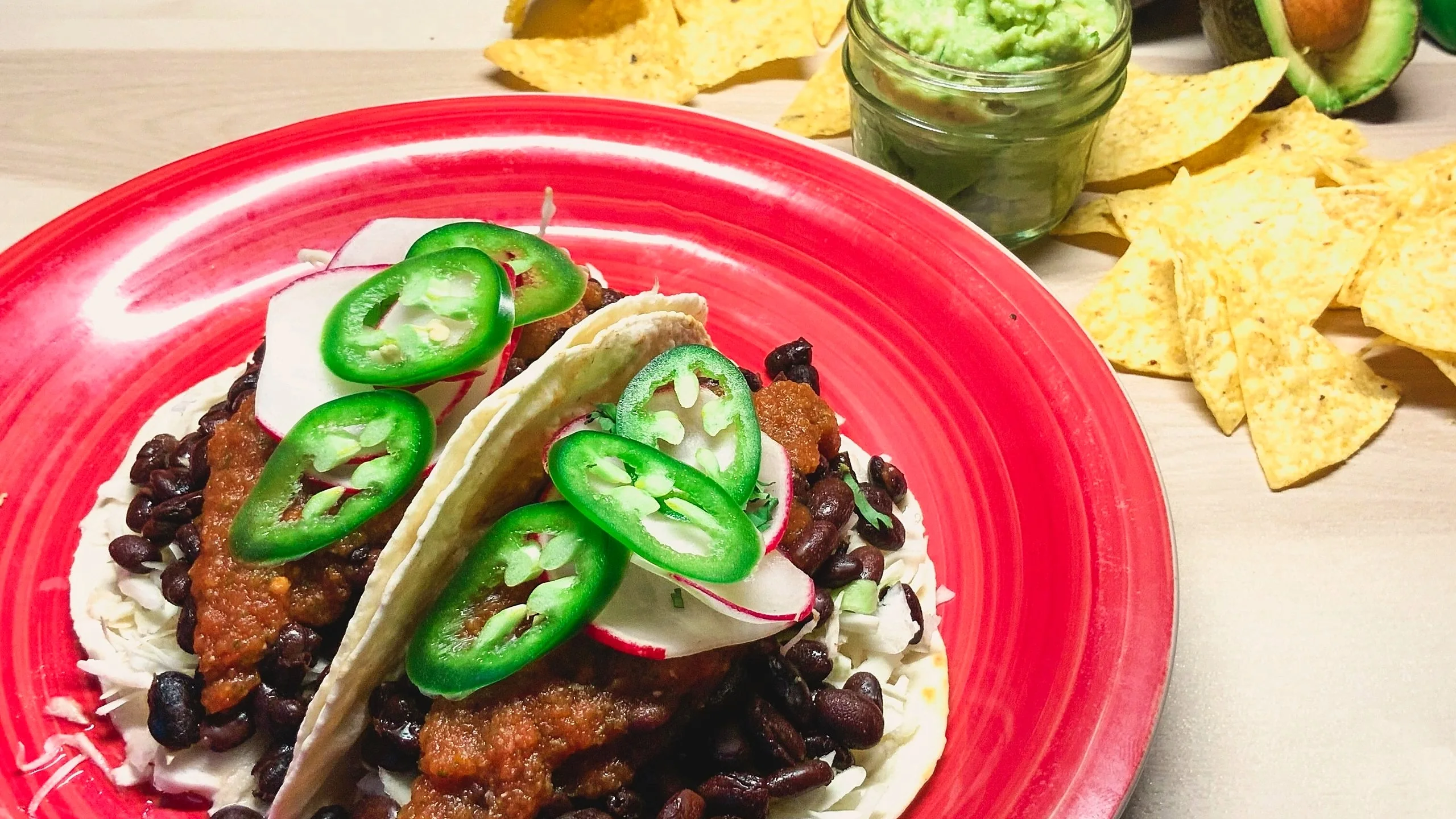 Rancheros tacos with black beans, salsa rojas, jalapeño and radish on a red plate