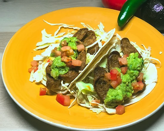 Chorizo tacos topped with guacamole and diced tomato on a yellow plate