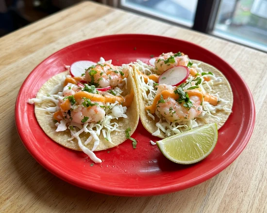 Two shrimp tacos with cabbage, radish, cilantro and a peach drizzle on a red plate